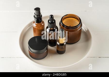 Set aus Kosmetikflaschen aus bernsteinfarbenem Glas auf einem Teller auf Holzgrund. Naturkosmetik ohne Markenverpackung Stockfoto