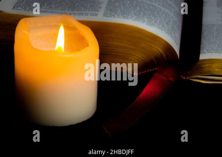 Alte Bibel mit goldenen Seiten, die von Kerzenlicht einer Kerze in der Nähe beleuchtet werden Stockfoto