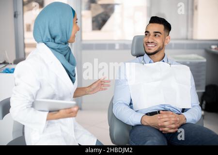 Glücklicher Arabischer Mann Und Muslimische Weibliche Zahnärzin Sprechen Während Des Checkup In Der Klinik Stockfoto
