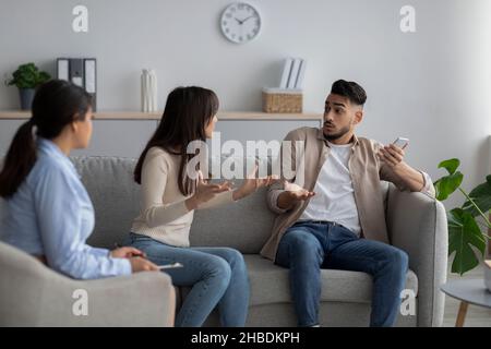 Wütende arabische Dame, die sich über die Smartphone-sucht ihres Mannes beschwert und bei der Konsultation des Psychologen sitzt Stockfoto