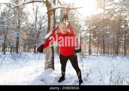 Bungee-Fitness im Freien. Ein starker, reifer Sportler, der im verschneiten Winterpark mit gefederten Trainingsgurten trainiert Stockfoto