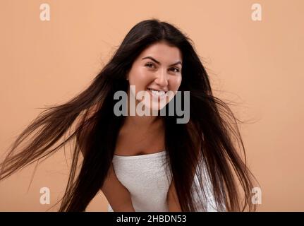 Haarpflegekonzept. Porträt einer glücklichen armenischen Frau mit fliegenden dunklen langen Haaren auf beigem Hintergrund Stockfoto