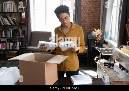 Glückliche junge afroamerikanische Frau, die Bücher aus der Schachtel auspackt. Stockfoto