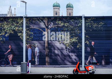 Eine große Plakatwand als Trennwand zu einer Baustelle am Münchner Marienhof für eine neue Eisenbahn. Der Turm der Münchner Frauenkirche im Hintergrund. Stockfoto