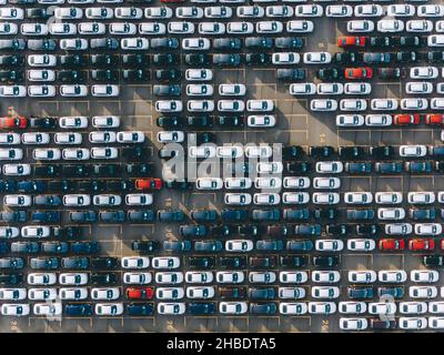 Offenes fertiges Automobillager eines riesigen Werks mit Reihen von Autos verschiedener Farben, die Schatten in der hellen Morgenansicht werfen Stockfoto