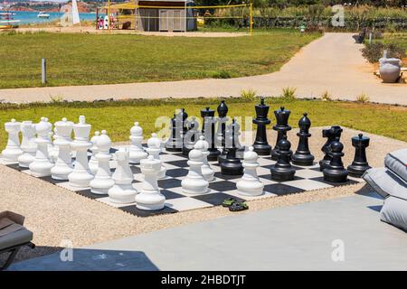Wunderschöne Aussicht auf das Schachbrett mit riesigen schwarz-weißen Schachfiguren zum Spielen im Freien am Strand. Griechenland. Stockfoto