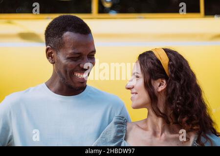 Der junge Afro-Amerikaner und die weiße Brünette gehen im sonnigen Sommer in der Nähe des Stadtparks miteinander lächelnd an Stockfoto