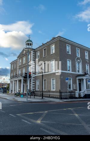 DUBLIN, IRLAND - 03. Nov 2021: Eine vertikale Aufnahme eines grauen Mehrfamilienhauses mit drei Geschäften unter dem klaren Himmel in Dublin, Irland Stockfoto