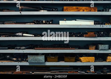 Regal mit Regalen in der Drehbank im Werk. Auf Regalen befinden sich Teile und Rohlinge für die Bearbeitung mit Metall. Industrieller Hintergrund. Länge Arbeitsplatz Wender. Stockfoto