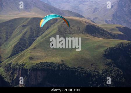 Ein Mann auf einem Gleitschirm macht ein Selfie. Bergschlucht mit grünen Hängen, ein Fallschirm mit Menschen fliegt über die Klippe. Wunderschöne Aussicht auf die Panoramalandschaft Stockfoto