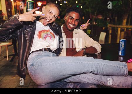Frieden mit Freunden. Zwei beste Freunde, die eine gute Zeit in einem Restaurant im Freien in der Stadt haben. Zwei glückliche junge Menschen genießen beim Hängen ein paar Biere Stockfoto