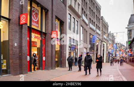 Amsterdam, Niederlande. 19 dez 2021. Menschen in kleinen Gruppen beobachten soziale Distanzierungen und schlendern durch die Kalverstraat, normalerweise eine der belebtesten Einkaufsstraßen Amsterdams, am ersten Tag der vollständigen Sperre. Ab Sonntag, dem 19th. Dezember, wird eine vollständige Sperrung durch die Regierung der Niederlande angekündigt. Nur wichtige Geschäfte können geöffnet bleiben und Gruppen von maximal 2 Personen über 13ys Jahren dürfen im Freien zusammenkommen, es sei denn, sie gehören demselben Haushalt an.Quelle: Steppeland/Alamy Live News Stockfoto