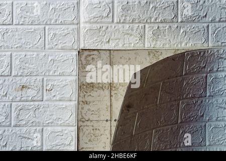 Die Tapete beginnt sich abzulösen. Die Tapete aus alten weißen Ziegeln schälte sich von der Wand im Raum, weil es feucht war oder sich nicht gut klebte. Reparieren Sie A Stockfoto