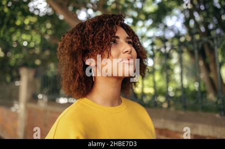 Sorglose Teenager-Mädchen suchen sich fröhlich im Freien. Selbstbewusste junge Frau, die rote Haare und ein Senf-Sweatshirt in der Stadt trägt. Junger Teenager Stockfoto