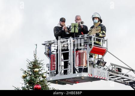 Barmstedt, Deutschland. 19th Dez 2021. Zwei Trompeter spielen Weihnachtslieder neben einem Feuerwehrmann im Korb einer Drehteller-Feuerwehrleiter auf dem Marktplatz in Barmstedt. Auch andere Feuerwehren im Kreis Pinneberg machen heute so Musik und werden gemeinsam eine gemeinsame Weihnachtsbotschaft aus Videoaufnahmen bearbeiten. Quelle: Markus Scholz/dpa/Alamy Live News Stockfoto