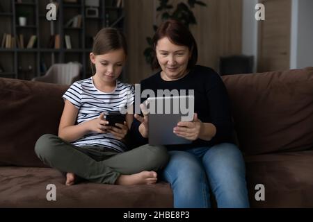 Die ältere Oma sitzt auf der Couch und die Enkelin hält das Tablet Stockfoto