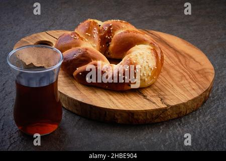 Türkisches Gebäck acma und Tee in traditionellem Teeglas auf Holzbrett bei dunklem Hintergrund Stockfoto