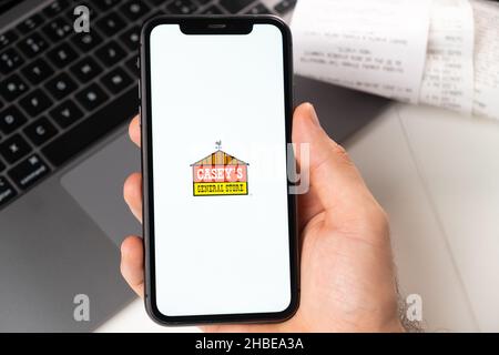 Caseys Anwendung von Supermarkt und Lebensmittelgeschäft in einem Smartphone. Ein Mann hält ein Smartphone mit App zum Einkaufen und einen Laptop im Hintergrund. November 2021, San Francisco, USA Stockfoto