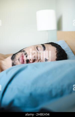 Porträt eines bärtigen halbschwarzen Mannes mit gemischter Rasse, der am Morgen auf einem hellblauen Kissen schläft. Junger Mann schläft friedlich Stockfoto