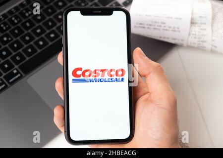 Costco Großhandel Anwendung von Supermarkt und Lebensmittelgeschäft in einem Smartphone. Ein Mann hält ein Smartphone mit App zum Einkaufen und einen Laptop im Hintergrund. November 2021, San Francisco, USA Stockfoto