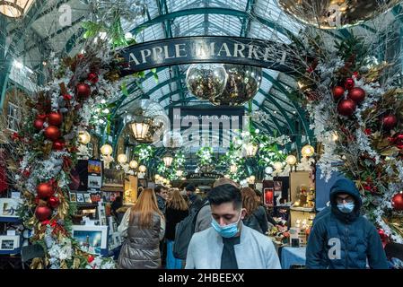 London, Großbritannien. 19. Dezember 2021. Menschen, die am letzten Einkaufswochenende vor Weihnachten Gesichtsmasken unter den Dekorationen auf dem Apple Market von Covent Garden tragen. Die Fälle der Omicron-Variante sind so stark angestiegen, dass die britische Regierung mit der Umsetzung strengerer Plan-C-Beschränkungen konfrontiert ist, um ihre Ausbreitung einzudämmen, wie zum Beispiel einem Verbot der Vermischung in Innenräumen zwischen Haushalten und einem Verbot der Innenbewirtung. Kredit: Stephen Chung / Alamy Live Nachrichten Stockfoto