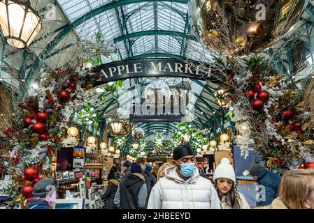 London, Großbritannien. 19. Dezember 2021. Menschen, die am letzten Einkaufswochenende vor Weihnachten Gesichtsmasken unter den Dekorationen auf dem Apple Market von Covent Garden tragen. Die Fälle der Omicron-Variante sind so stark angestiegen, dass die britische Regierung mit der Umsetzung strengerer Plan-C-Beschränkungen konfrontiert ist, um ihre Ausbreitung einzudämmen, wie zum Beispiel einem Verbot der Vermischung in Innenräumen zwischen Haushalten und einem Verbot der Innenbewirtung. Kredit: Stephen Chung / Alamy Live Nachrichten Stockfoto