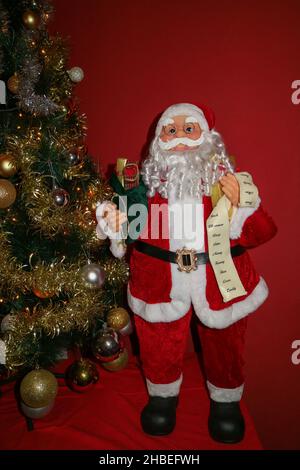 Weihnachtsmann mit einem weißen langen Bart, rotem Hut, Brille und einer grünen Tasche voller Geschenke, Weihnachtsmann und Weihnachtsbaum mit Dekoration, Weihnachtsmann Kind Stockfoto