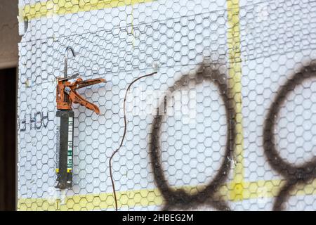 Culk gun hängt an einer Wand mit Metallkonstruktion Mesh in der Nähe Spray lackiert Symbole bedeckt Stockfoto