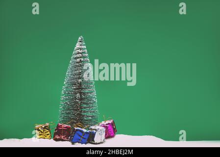 Kiefernbaum auf mattgrünem Hintergrund mit etwas Schnee und Geschenkschachteln. Stockfoto