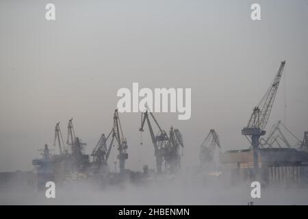 Der Bau von nuklearen Eisbrechern, Kräne der baltischen Werft in einem frostigen Wintertag, Dampf über dem Fluss Neva, glatte Oberfläche der Stockfoto