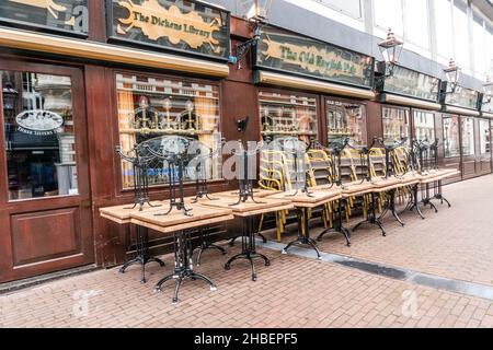 Amsterdam, Niederlande. 19 dez 2021. Vor der „Dickens Library“, einem Pub in der Nähe des Rembrand Square, stapelten sich Tische und Stühle auf der Terrasse. Ab Sonntag, dem 19th. Dezember, wird eine vollständige Sperrung durch die Regierung der Niederlande angekündigt. Mit dem harten Lockdown sind neben den nicht notwendigen Geschäften auch die Gastronomie, Kinos, Theater und Zoos geschlossen. Für viele Unternehmen findet die Schließung genau in den wichtigsten Wochen des Jahres statt. Kredit: Steppeland/Alamy Live Nachrichten Stockfoto
