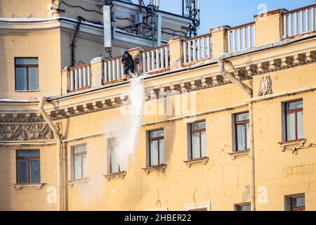 Russland, St. Petersburg, 07. Dezember 2021: Die Arbeit der Versorgungsunternehmen, um Schnee von den Dächern von Häusern zu entfernen, wirft ein Mann den Schnee vom Dach, ist er Stockfoto