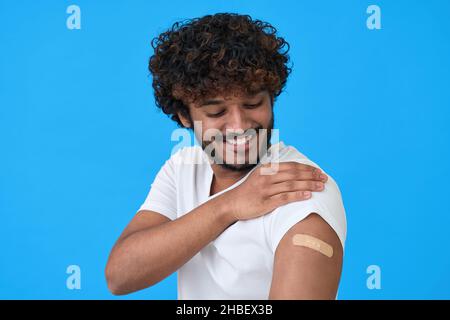 Glücklicher junger indischer Mann, der nach einer blauen Impfung einen Verband am Arm zeigt. Stockfoto