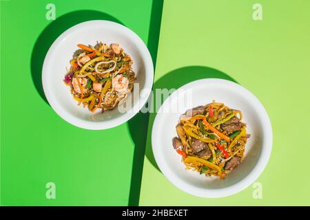 Zwei Teller mit Nudeln mit Meeresfrüchten und Huhn auf grün Stockfoto