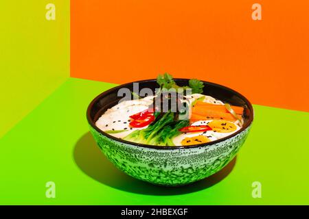 Ramen asiatische Nudel in Brühe mit Rindfleisch Zunge Fleisch, Pilz und eingelegtes Ei in Schüssel auf grünem und orangefarbenem Hintergrund Stockfoto