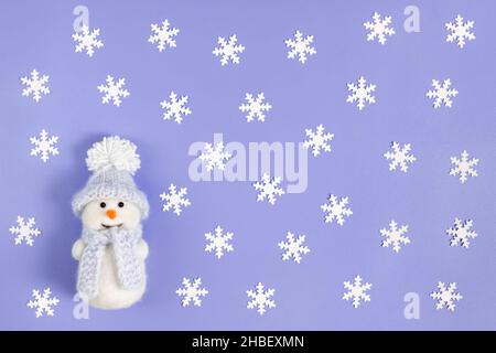 Weihnachtliche Komposition mit weißen Schneeflocken und einem niedlichen Schneemann auf violettem Hintergrund. Farbe des Jahres 2022 sehr Peri. Draufsicht, flach liegend. Stockfoto