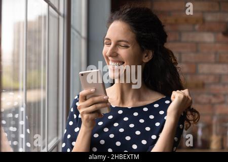 Emotionale glückliche junge lateinerin feiert Online-Erfolg. Stockfoto