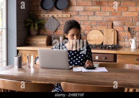 Konzentrierte junge hispanische Frau, die die Inlandsausgaben berechnet. Stockfoto