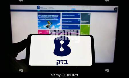 Person, die Mobiltelefon mit dem Logo von Bezeq, der israelischen Telekommunikationsgesellschaft, auf dem Bildschirm vor der Webseite hält. Konzentrieren Sie sich auf die Telefonanzeige. Stockfoto