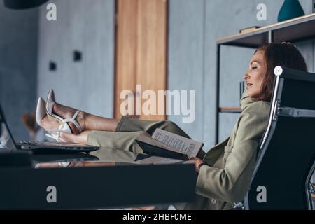 Die Frau sitzt mit den Füßen auf ihrem Schreibtisch. Stockfoto