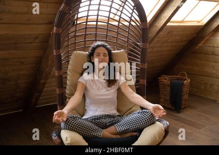 Glückliche junge hispanische Frau meditiert in einem bequemen Sessel. Stockfoto