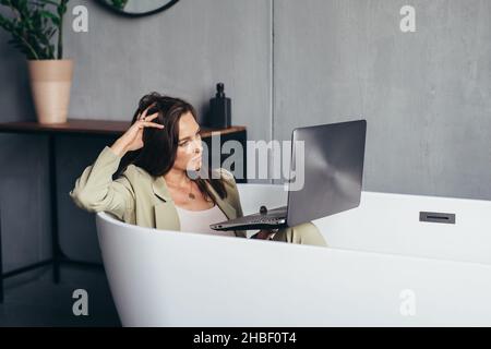 Frau arbeitet in der Badewanne mit ihrem Laptop in der Privatsphäre ihres Zuhauses. Stockfoto