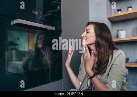 Frau genießt den Duft von Gebäck, das am Ofen sitzt. Stockfoto