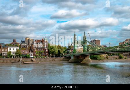 Riverside Häuser in Hammersmith, West London, England, mit der historischen Hammersmith Bridge, die die Themse überquert, auf der rechten Seite. Stockfoto