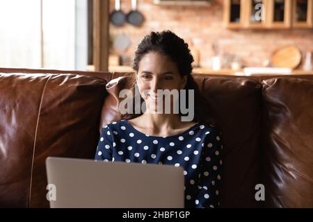 Lächelnd attraktive tausendjährige hispanische Frau, die am Computer arbeitet. Stockfoto
