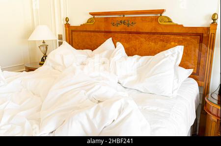 Ungeschmachtes Bett mit zerknitterter Bettwäsche, Bettwäsche und Laken in einem leeren, luxuriösen Hotelzimmer Stockfoto