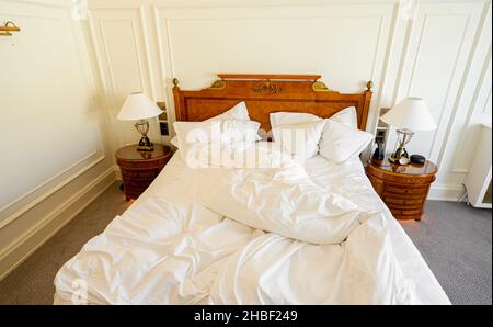 Ungeschmachtes Bett mit zerknitterter Bettwäsche, Bettwäsche und Laken in einem leeren, luxuriösen Hotelzimmer Stockfoto