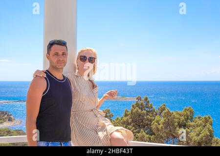 Junge Familie, eine Frau umarmt einen Mann in einem Pavillon mit Blick auf das blaue Meer. Reisen und Tourismus im Sommer. Speicherplatz kopieren. Stockfoto