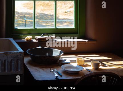 Alte Zeiten Bauernhaus Interieur in einer Küche. Ländliche Wohnküche mit abgenutztem Holztisch und Rührschüssel, Löffel, Gabel, Teller Stockfoto