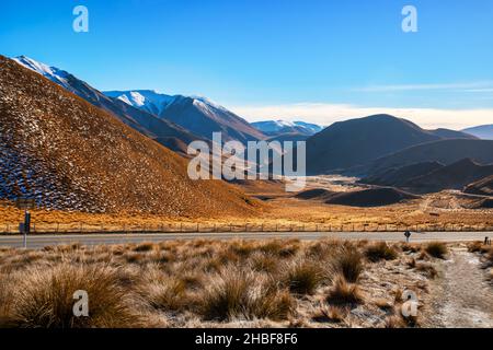 Auf der Fahrt durch das goldene Stoßzäungelände des Alpenpasses mit einem Schneegestäuber auf den Hügeln Stockfoto